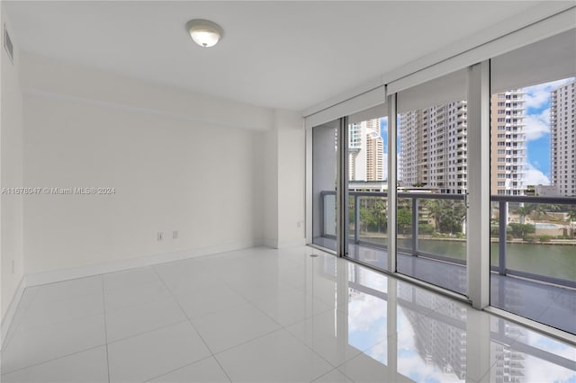 empty room featuring floor to ceiling windows, light tile patterned flooring, and a water view