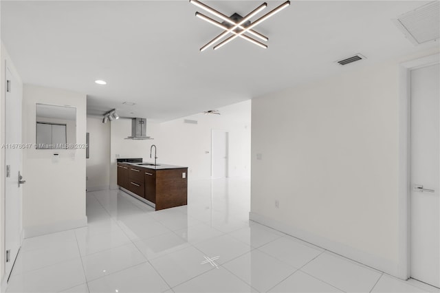 kitchen featuring wall chimney range hood, sink, an island with sink, dark brown cabinets, and light tile patterned floors