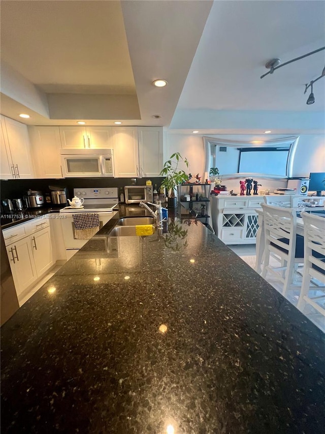 kitchen featuring white cabinets, dark stone counters, and white appliances