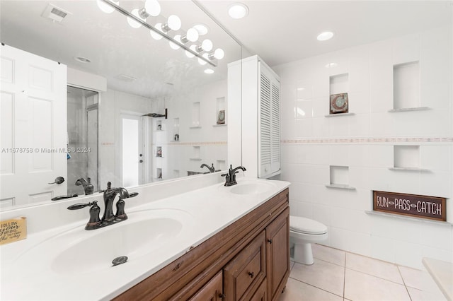 bathroom with toilet, tile patterned flooring, vanity, tile walls, and a tile shower