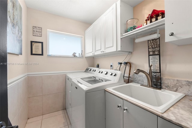 clothes washing area with cabinets, light tile patterned floors, washer and dryer, tile walls, and sink