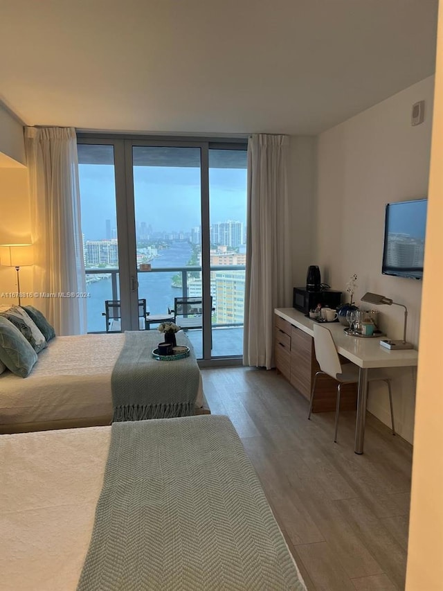 bedroom with a water view, hardwood / wood-style flooring, access to outside, and a wall of windows