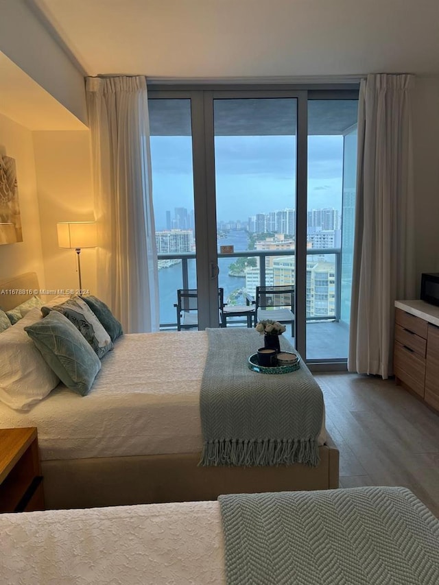 bedroom with a water view, hardwood / wood-style flooring, access to outside, and floor to ceiling windows