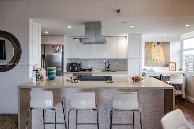 kitchen featuring range hood, white cabinetry, sink, and stainless steel refrigerator