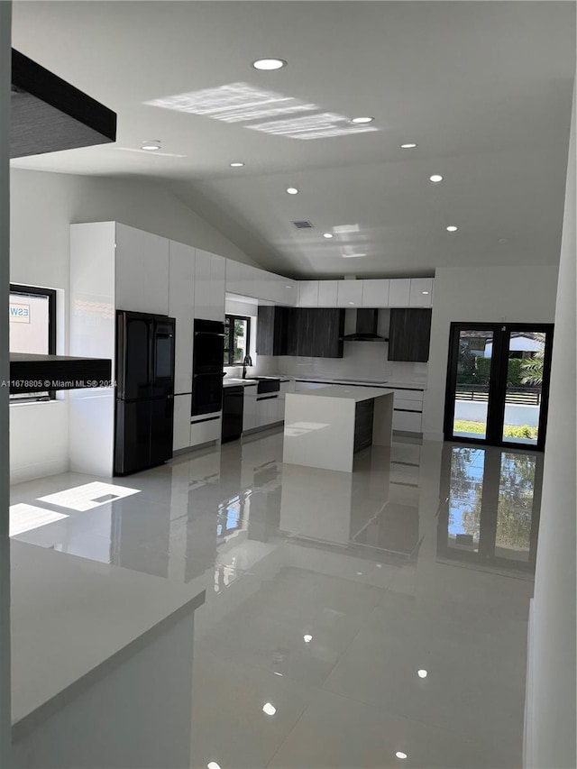 kitchen with wall chimney range hood, white cabinets, vaulted ceiling, light tile patterned flooring, and black appliances