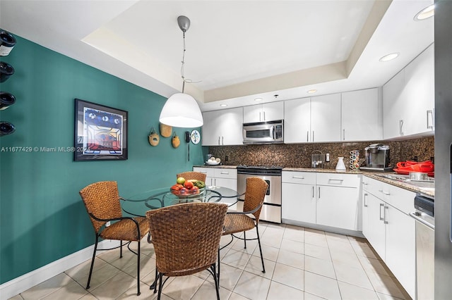 kitchen with stainless steel appliances, a tray ceiling, decorative light fixtures, white cabinetry, and tasteful backsplash