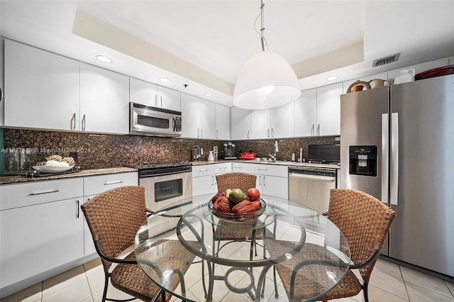 kitchen featuring white cabinets, tasteful backsplash, hanging light fixtures, light tile patterned flooring, and stainless steel appliances