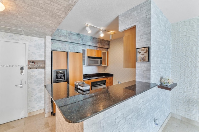 kitchen featuring kitchen peninsula, track lighting, light tile patterned floors, appliances with stainless steel finishes, and dark stone countertops