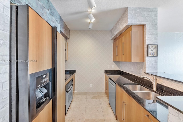 kitchen with appliances with stainless steel finishes, sink, a textured ceiling, dark stone countertops, and track lighting