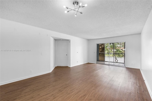 unfurnished room featuring a textured ceiling, dark hardwood / wood-style flooring, and an inviting chandelier