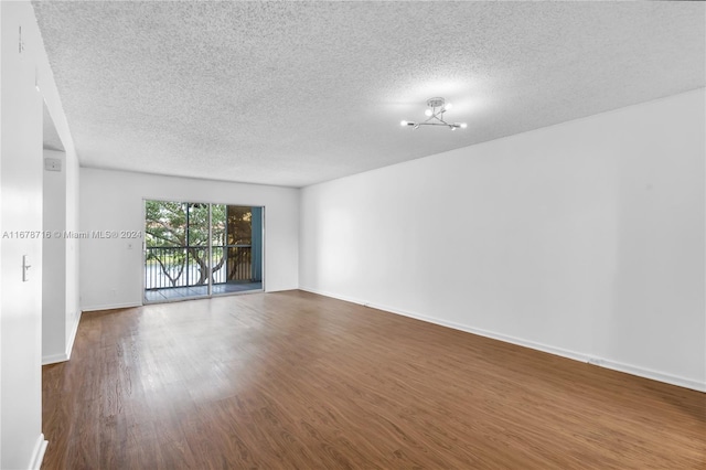 spare room with a textured ceiling, a chandelier, and dark wood-type flooring