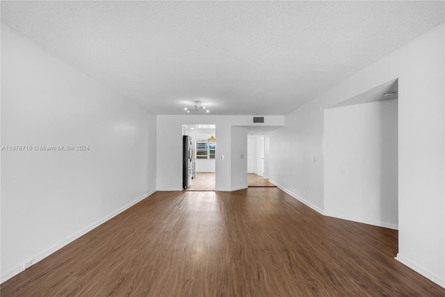 spare room featuring dark wood-type flooring, a textured ceiling, and a chandelier