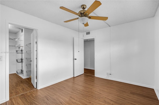 unfurnished bedroom with a spacious closet, a textured ceiling, hardwood / wood-style floors, a closet, and ceiling fan