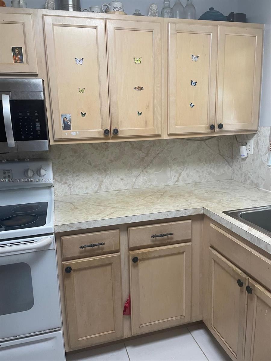 kitchen featuring tasteful backsplash, light tile patterned flooring, light brown cabinets, and white range