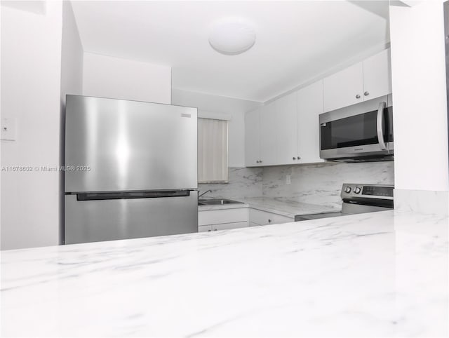 kitchen featuring white cabinets, appliances with stainless steel finishes, tasteful backsplash, sink, and light stone counters