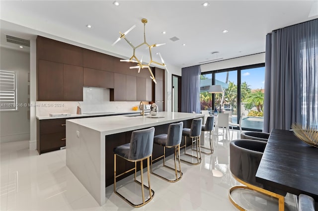 kitchen featuring tasteful backsplash, hanging light fixtures, an inviting chandelier, a kitchen island with sink, and sink