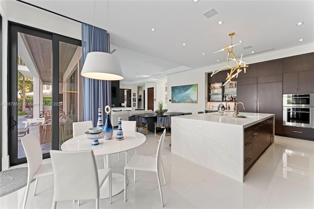 kitchen with dark brown cabinetry, light tile patterned flooring, pendant lighting, and a large island with sink