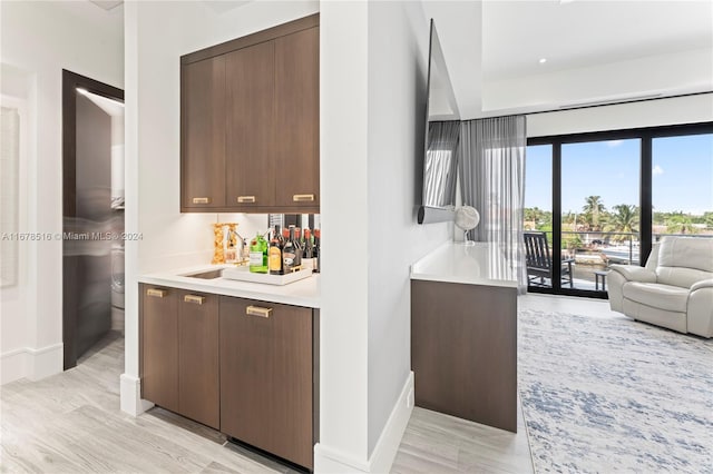 bar with dark brown cabinetry and light hardwood / wood-style floors