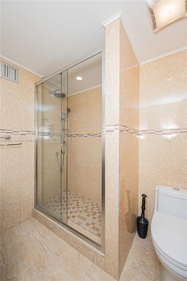 bathroom featuring toilet, an enclosed shower, and tile walls