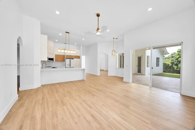 unfurnished living room with ceiling fan with notable chandelier and light wood-type flooring