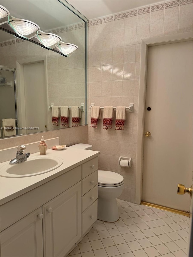 bathroom featuring a shower with door, tile patterned floors, toilet, vanity, and tile walls