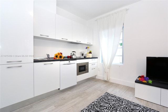 kitchen featuring stainless steel microwave, white dishwasher, sink, light wood-type flooring, and white cabinetry