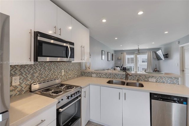 kitchen with kitchen peninsula, tasteful backsplash, appliances with stainless steel finishes, white cabinetry, and sink