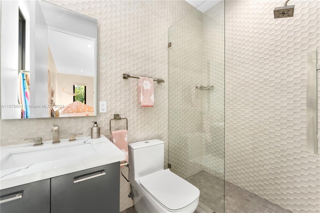 bathroom featuring vanity, toilet, tiled shower, and tile walls