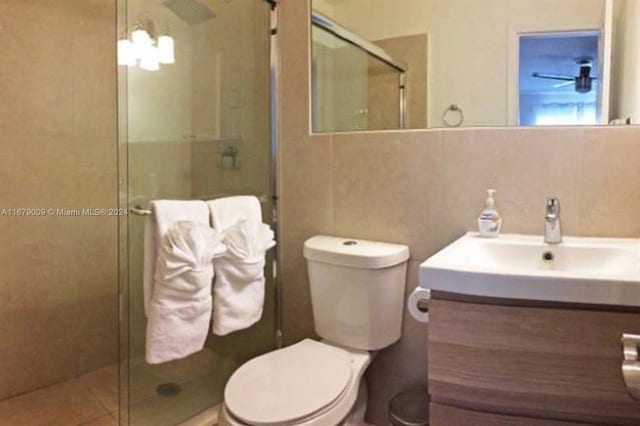 bathroom featuring a shower with door, tasteful backsplash, toilet, tile walls, and vanity