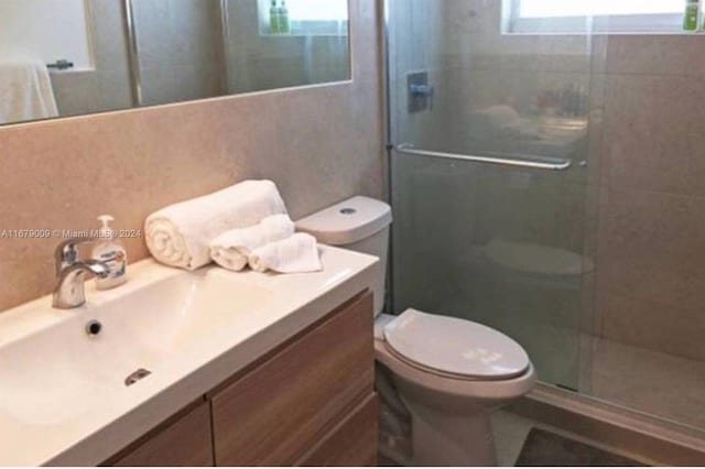 bathroom featuring toilet, vanity, and a shower with door