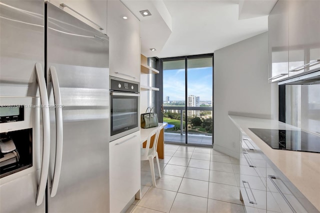 kitchen with white cabinets, light tile patterned floors, a wall of windows, and appliances with stainless steel finishes