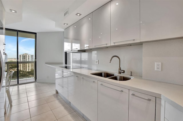 kitchen with sink, a wall of windows, backsplash, black electric stovetop, and white cabinets