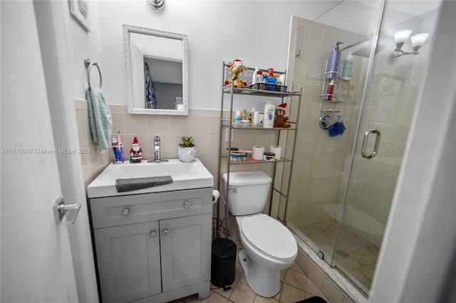 bathroom featuring vanity, a shower with door, tile patterned floors, toilet, and tile walls