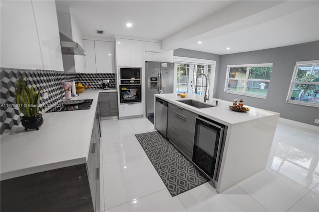 kitchen with wall chimney exhaust hood, a kitchen island with sink, sink, white cabinets, and wine cooler