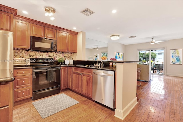 kitchen featuring kitchen peninsula, light wood-type flooring, sink, and black appliances