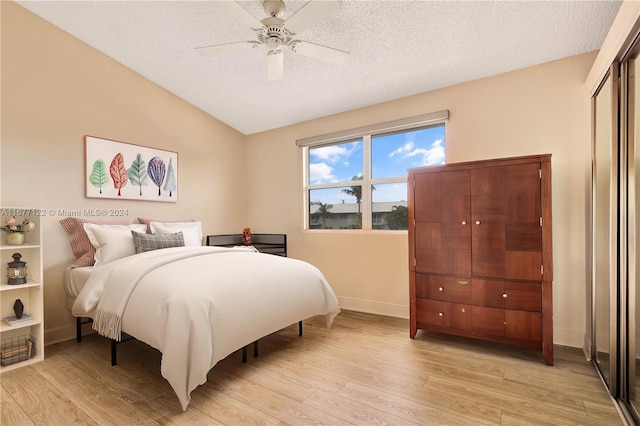 bedroom with lofted ceiling, ceiling fan, a textured ceiling, light wood-type flooring, and a closet