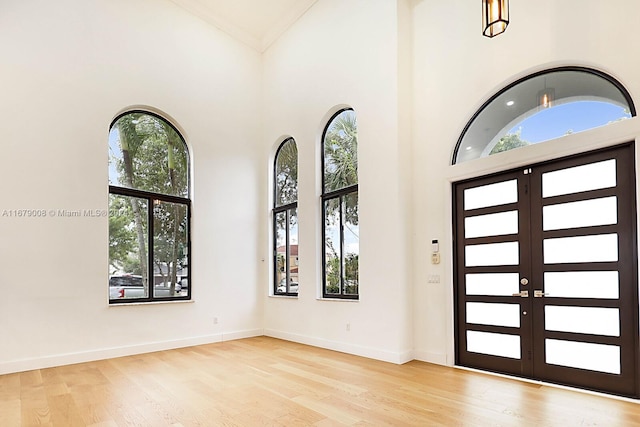 foyer with a high ceiling, crown molding, light wood-type flooring, and french doors