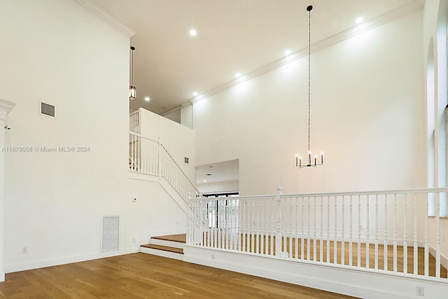 stairway with crown molding, hardwood / wood-style flooring, a chandelier, and a high ceiling