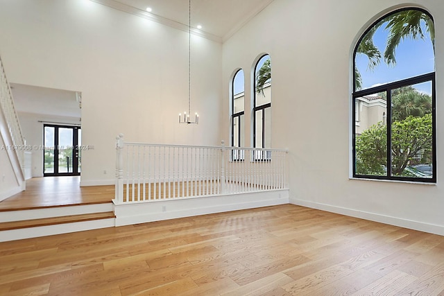 empty room with light hardwood / wood-style floors, ornamental molding, plenty of natural light, and a towering ceiling