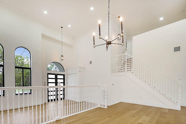 interior space with french doors, a towering ceiling, wood-type flooring, and an inviting chandelier