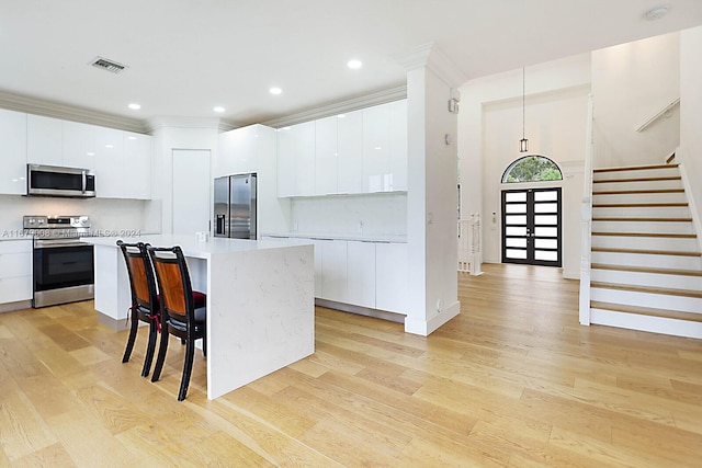 kitchen with a kitchen island, white cabinetry, stainless steel appliances, and light wood-type flooring