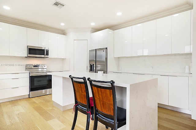 kitchen featuring a kitchen island, appliances with stainless steel finishes, white cabinetry, light wood-type flooring, and ornamental molding