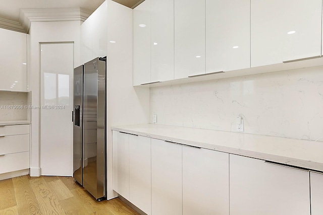 kitchen with stainless steel fridge, white cabinetry, ornamental molding, light hardwood / wood-style floors, and light stone counters