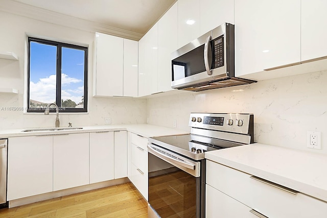 kitchen with sink, light wood-type flooring, white cabinetry, stainless steel appliances, and crown molding