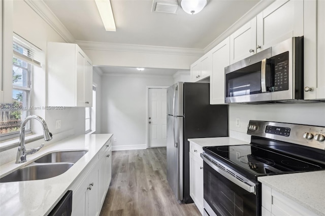 kitchen with appliances with stainless steel finishes, white cabinetry, ornamental molding, light hardwood / wood-style floors, and sink