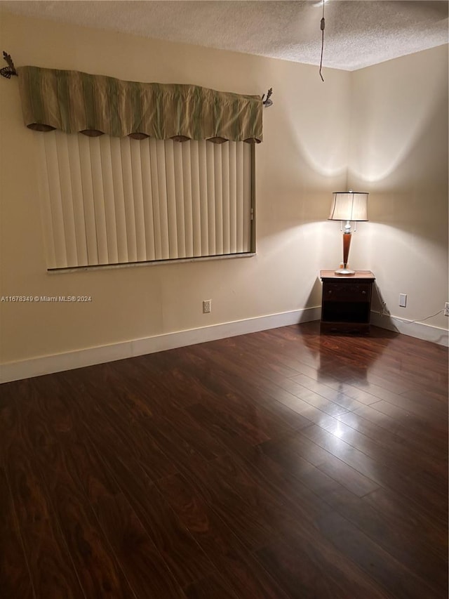 spare room featuring a textured ceiling and dark hardwood / wood-style floors