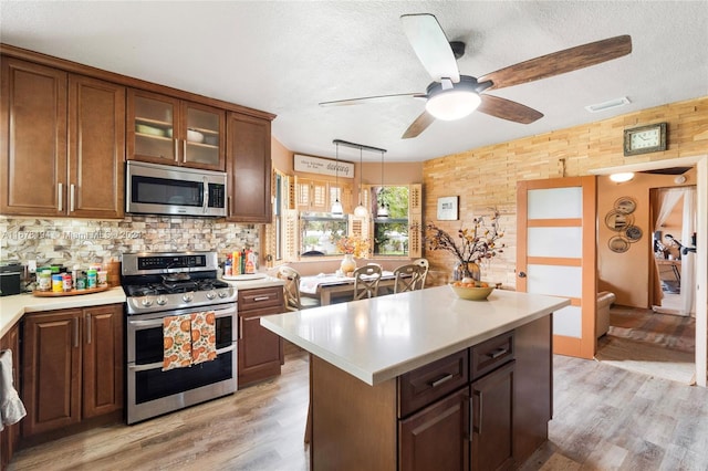 kitchen with a textured ceiling, stainless steel appliances, light wood-type flooring, and pendant lighting