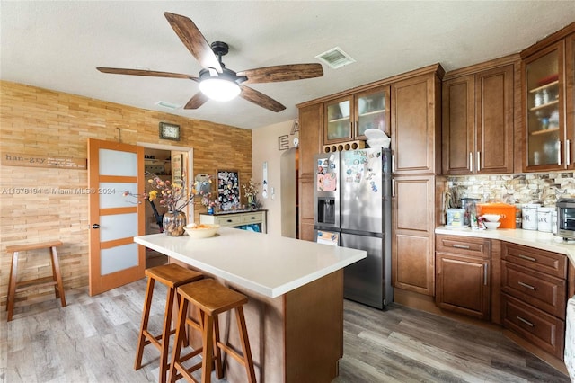 kitchen with a kitchen island, stainless steel refrigerator with ice dispenser, light hardwood / wood-style floors, and wooden walls