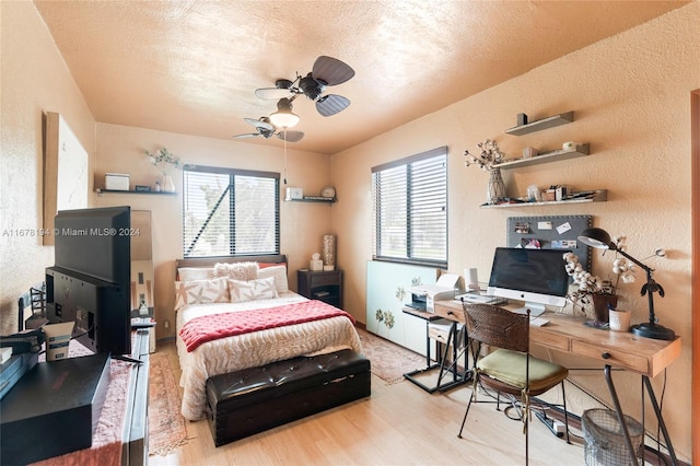 bedroom featuring ceiling fan, a textured ceiling, multiple windows, and light wood-type flooring