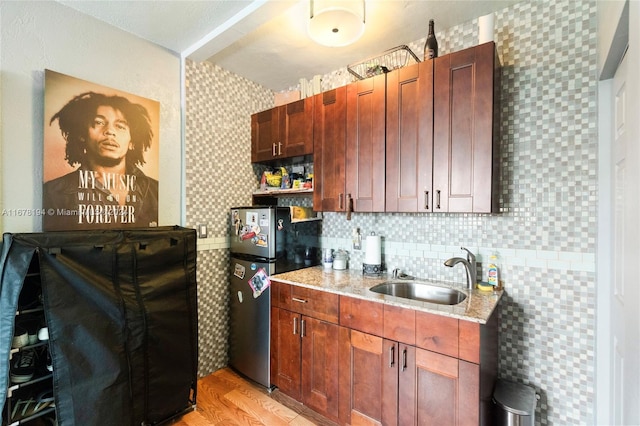 kitchen with decorative backsplash, stainless steel fridge, light stone countertops, light hardwood / wood-style floors, and sink